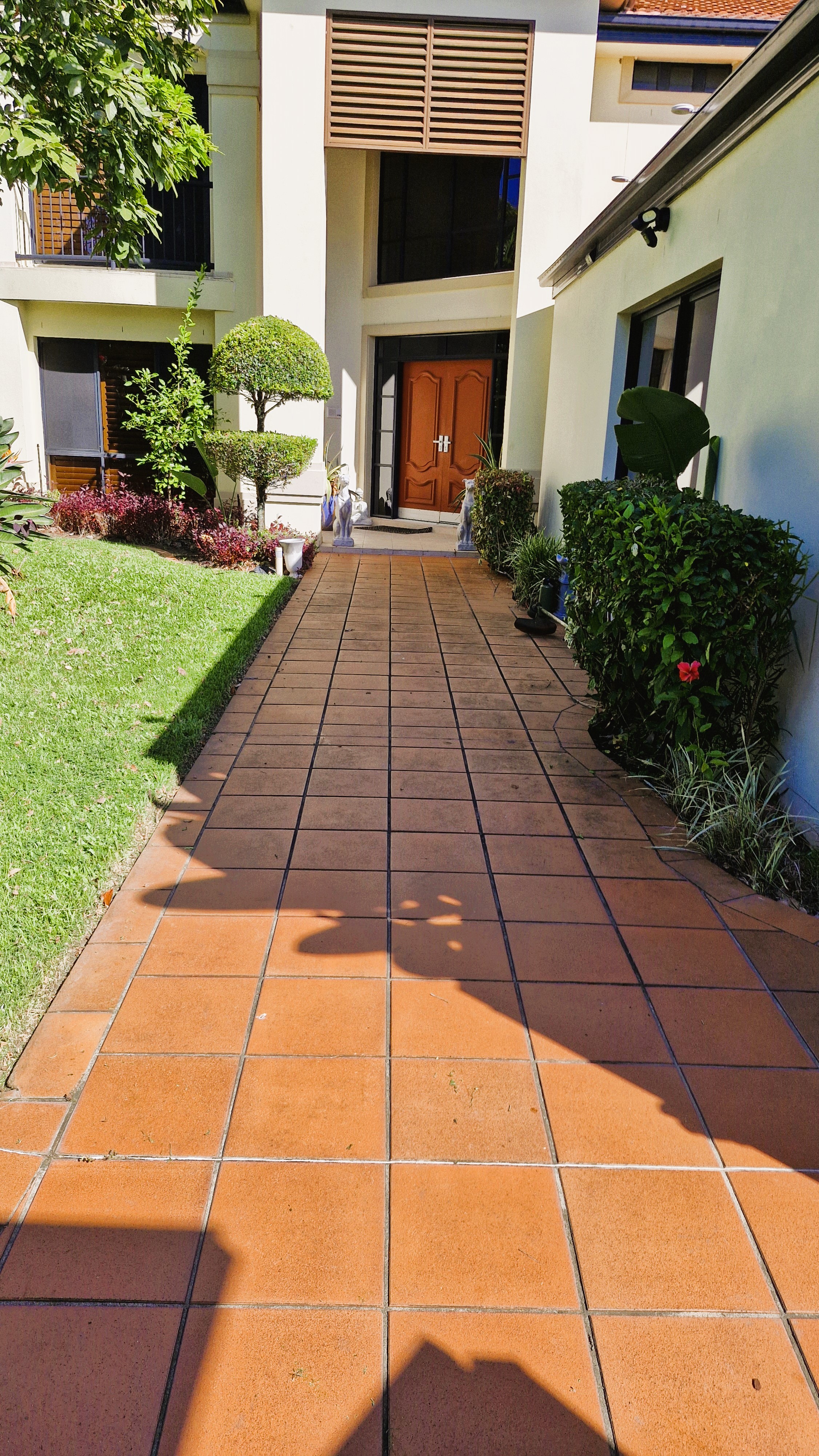 Tiled entrance walkway with shaped hedges, tropical plants, and pristine lawn at a prestige two-storey property