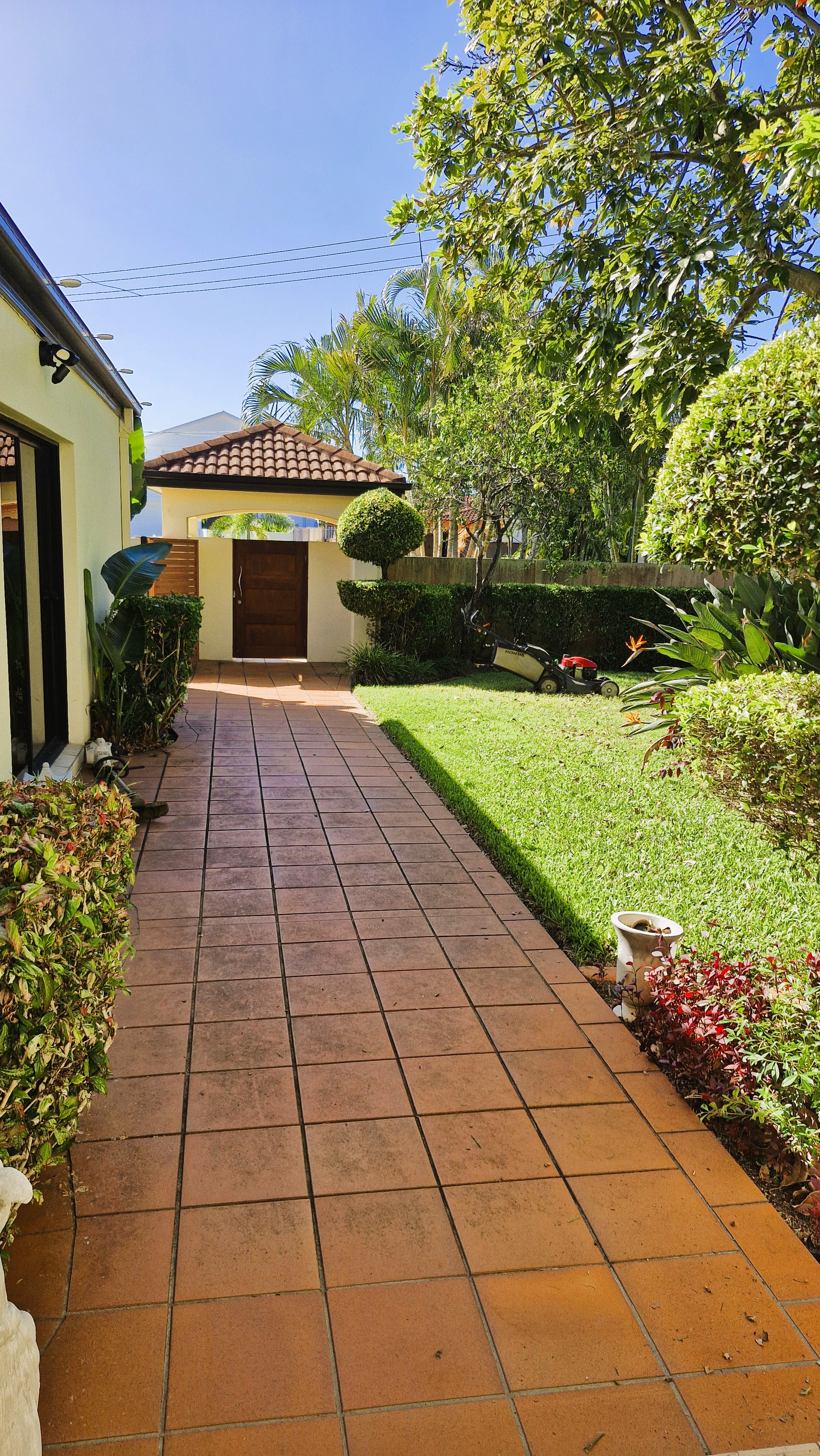 Manicured front garden with sculpted topiary, trimmed hedges, and lush lawn along a tiled pathway leading to a luxury Gold Coast home