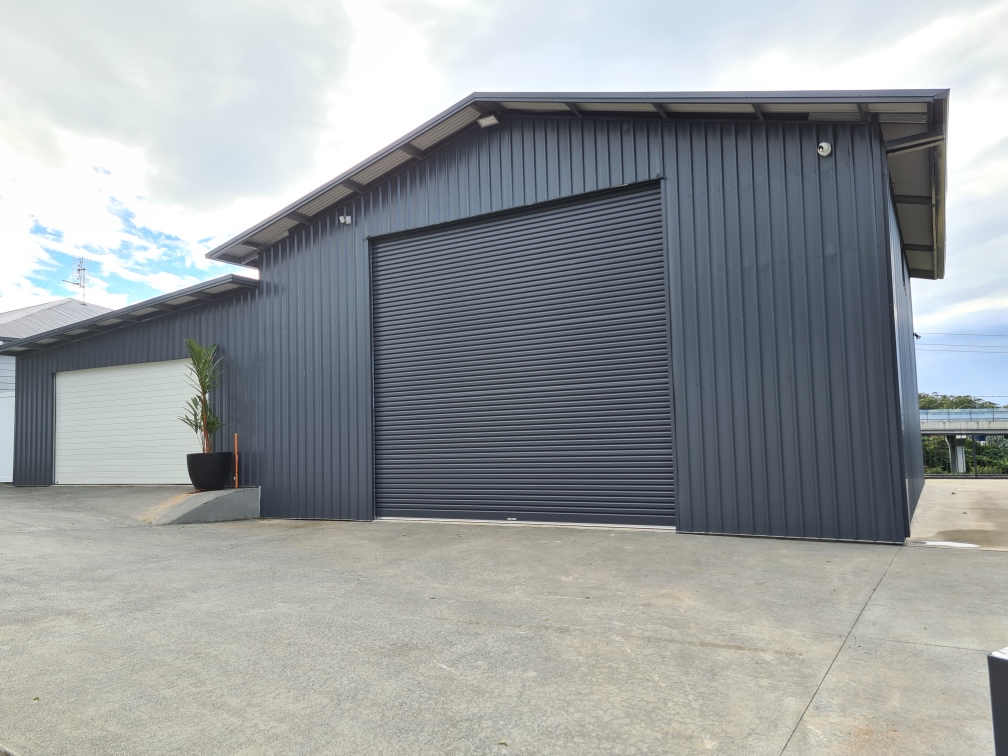 Dark charcoal steel commercial workshop with a large roller door and a second white door bay