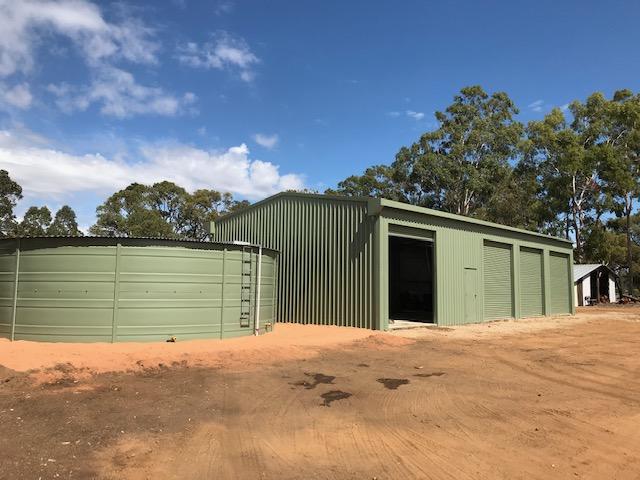 Green steel rural shed with roller doors next to a matching water tank