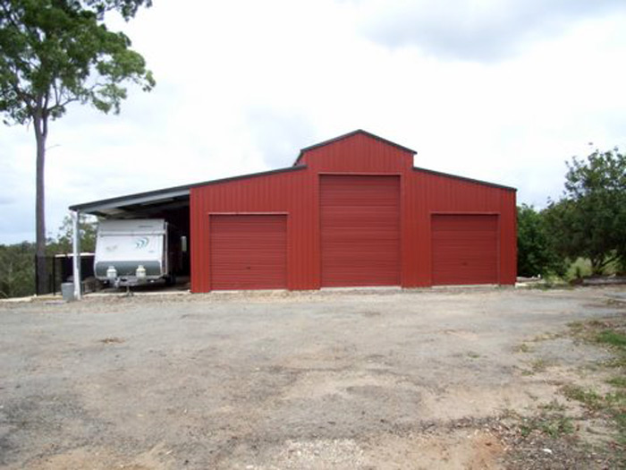 Red American barn with three roller doors and a lean-to carport on one side