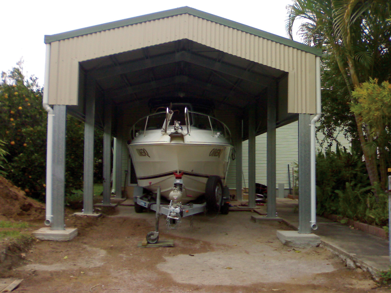 Tall open steel carport sheltering a boat on its trailer