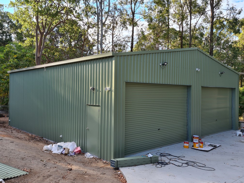 Green steel workshop with two roller doors and a personal-access door
