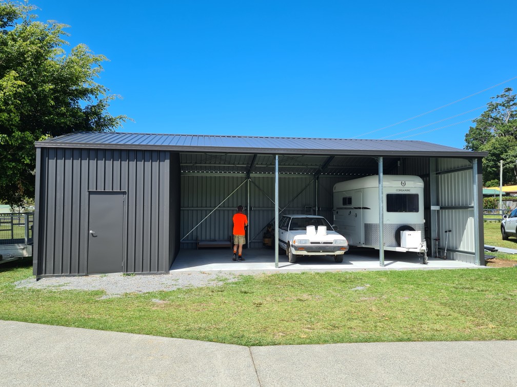 Open-front steel shed bay with a car and a horse float, and an enclosed storeroom at one end