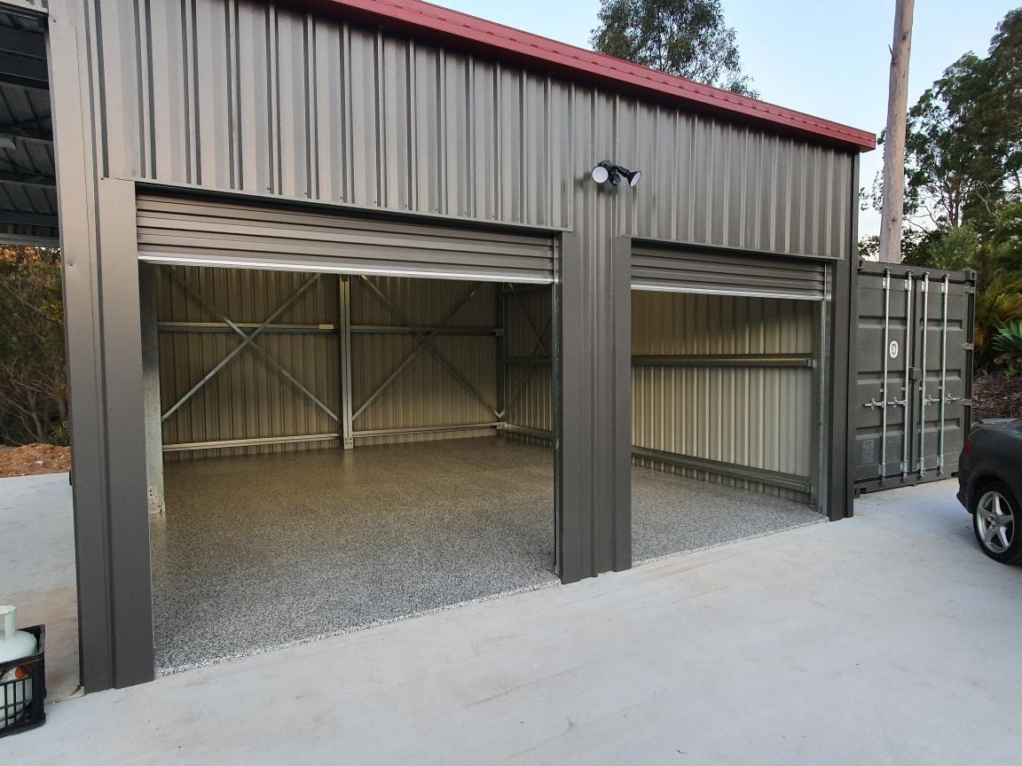 Grey steel building with two roller doors and red roof trim