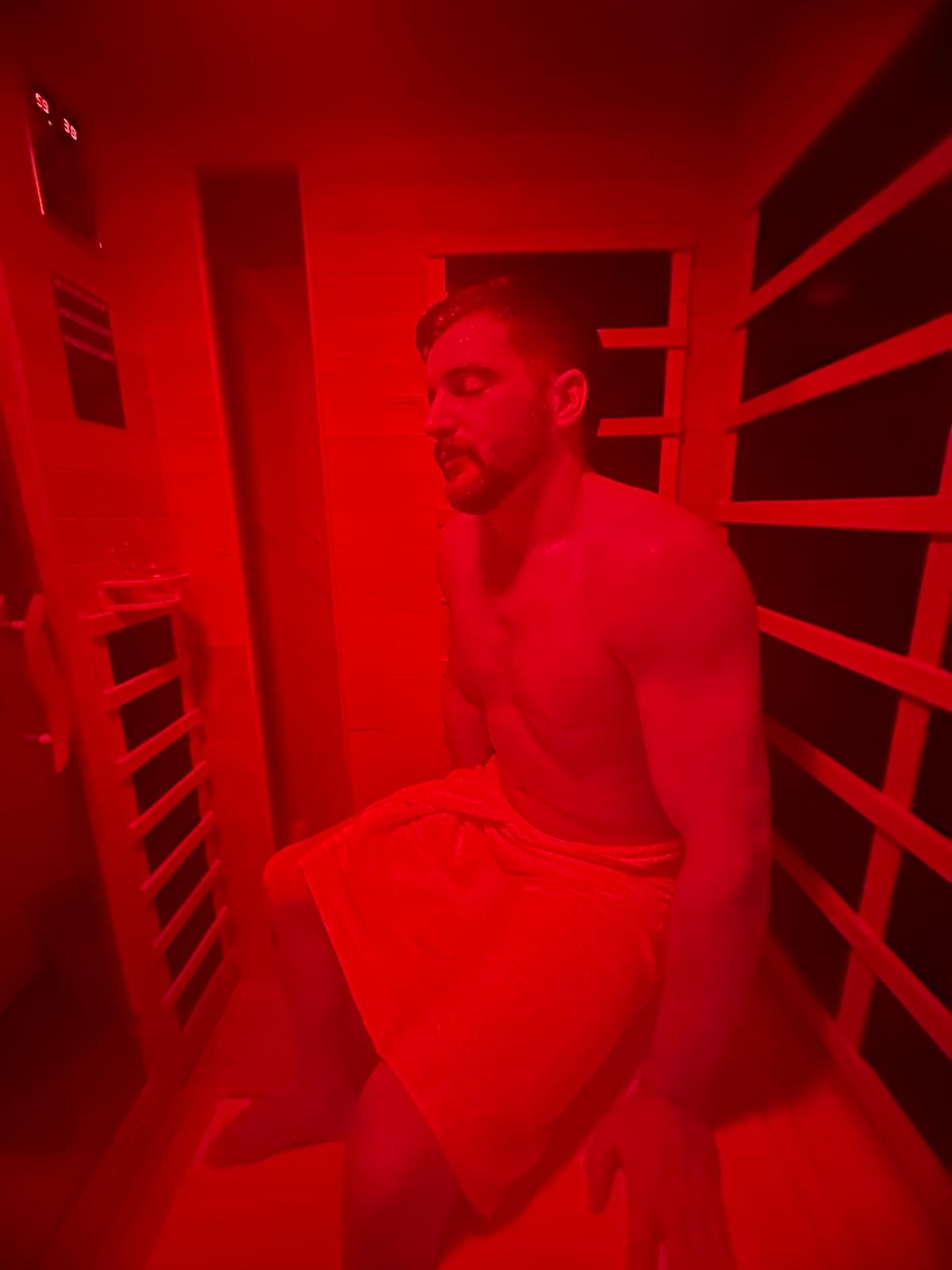 Man relaxing in infrared sauna with deep red glow at Realuxe Wellness