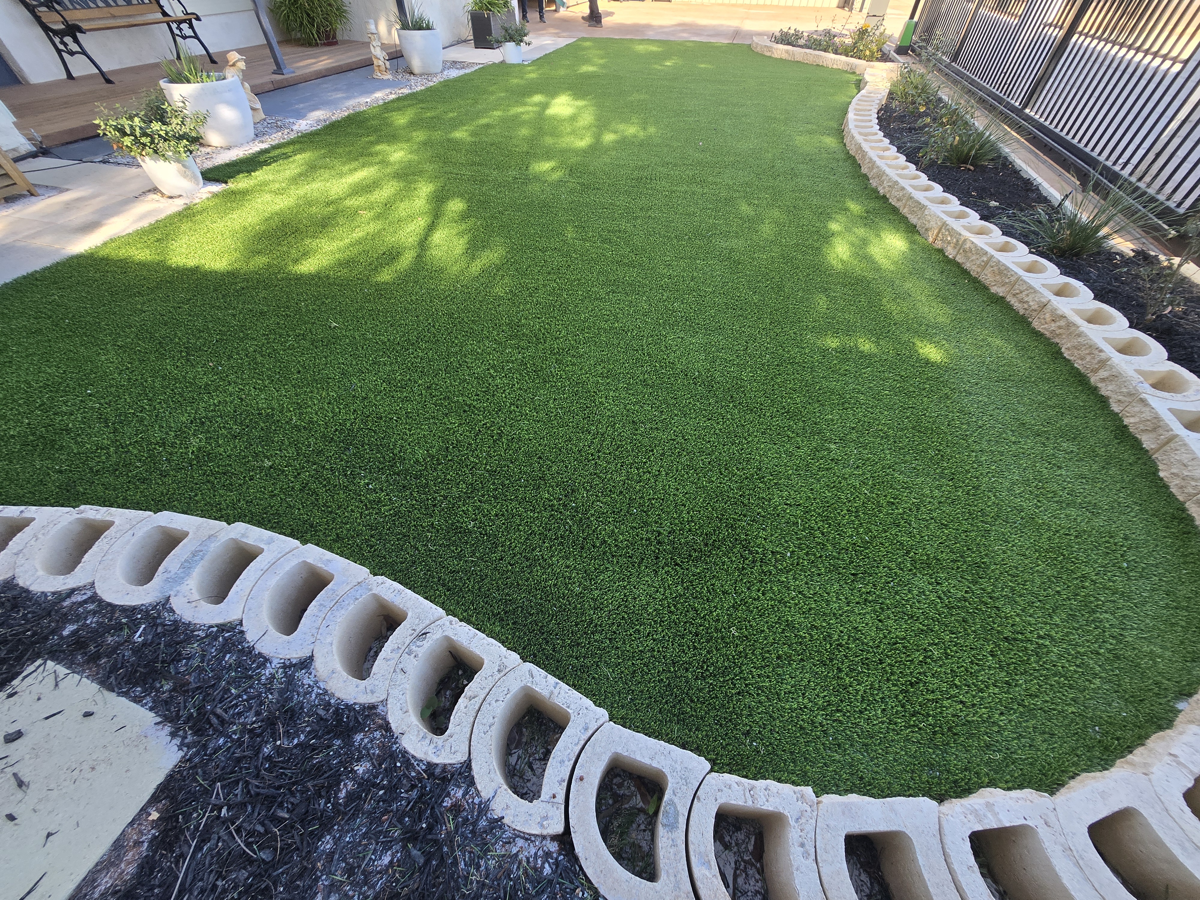 Curved synthetic lawn with decorative concrete block edging and garden beds in the Perth and Goldfields region