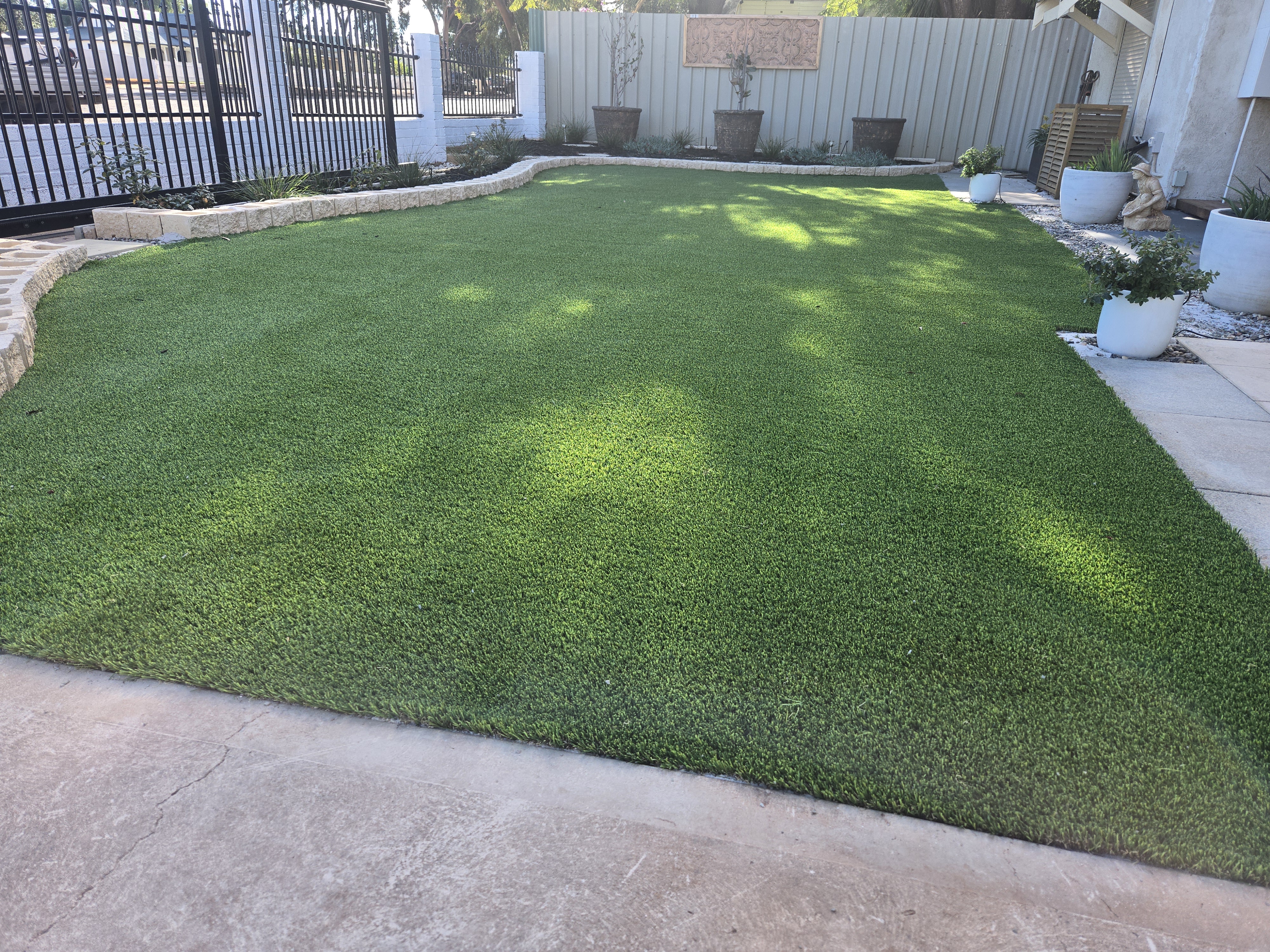 Synthetic lawn installation with stone retaining wall edging and Colourbond fencing in the Perth and Goldfields region