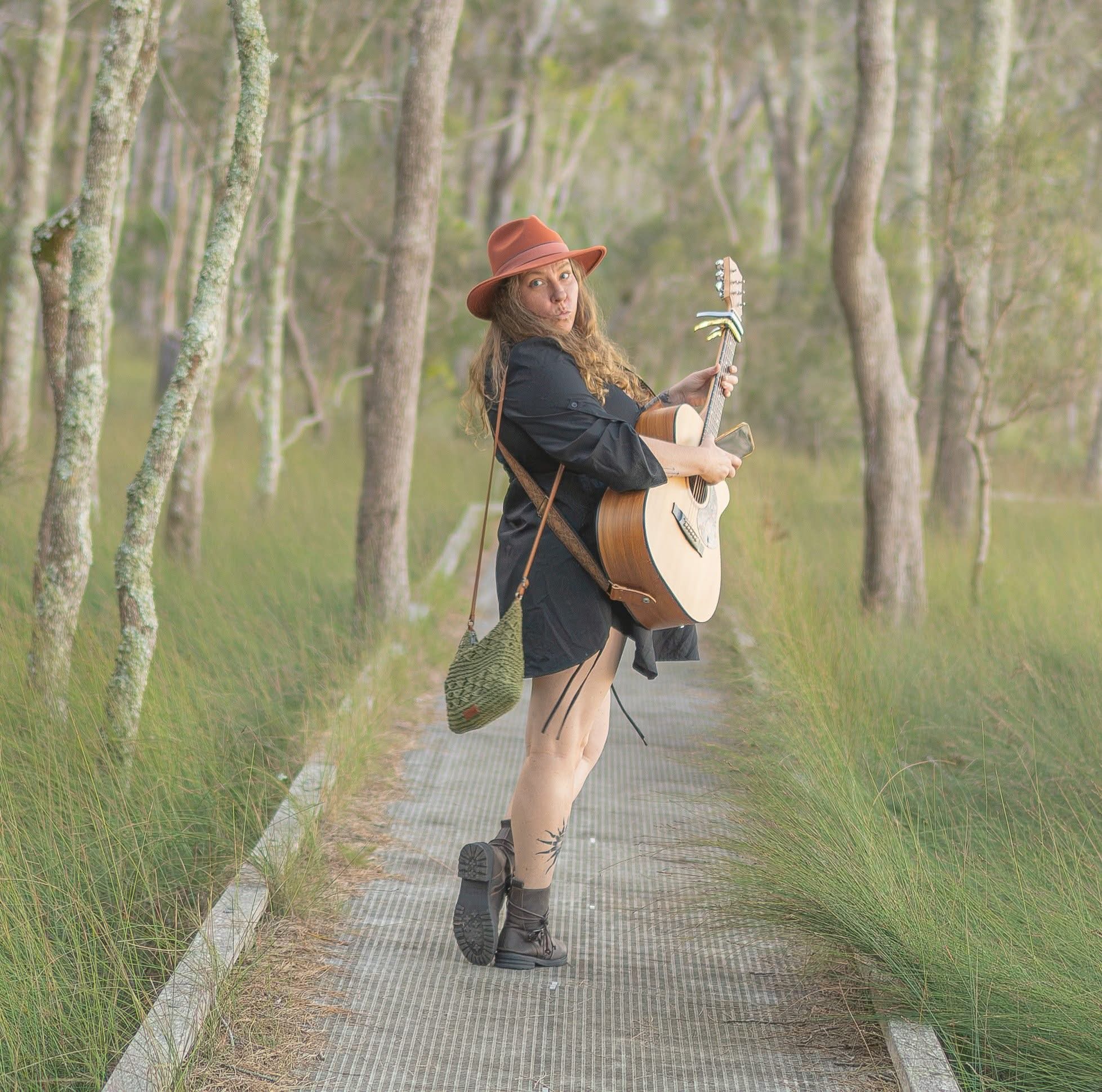 Shan Kae walking through Australian bushland with guitar