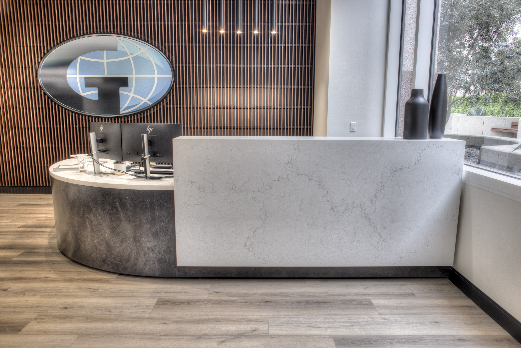 Custom reception desk with curved solid surface and wood slat accent wall for AJ Gallagher office tenant improvement in Los Angeles CA